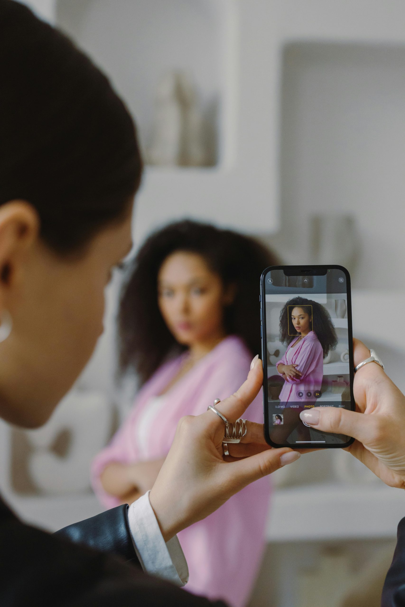 Two women capturing a portrait using a smartphone indoors.